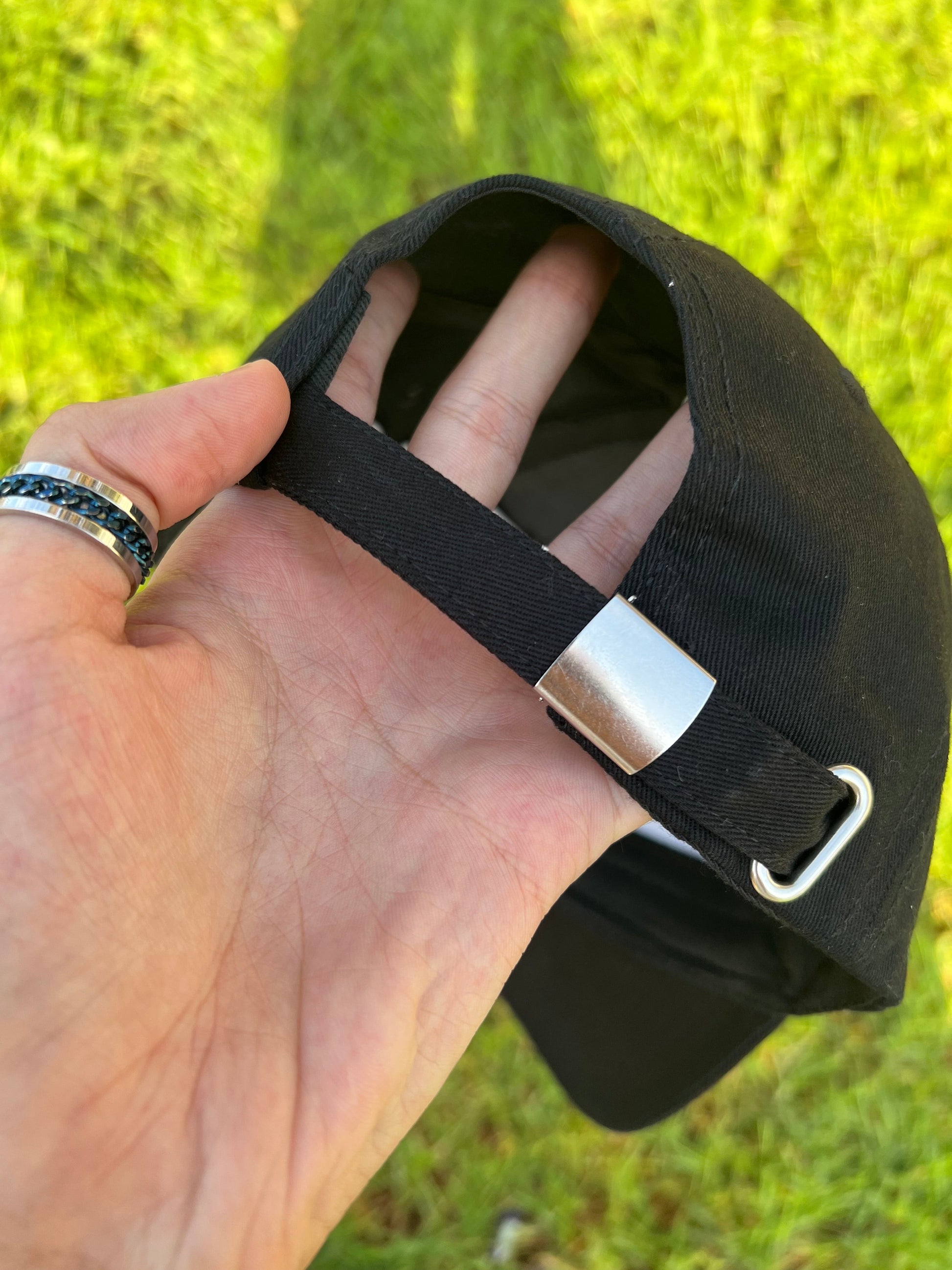 Hand holding a black cap with a metal clasp against a grassy background