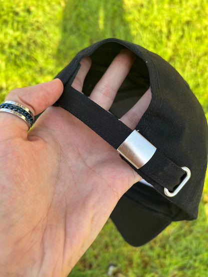 Hand holding a black cap with a metal clasp against a grassy background